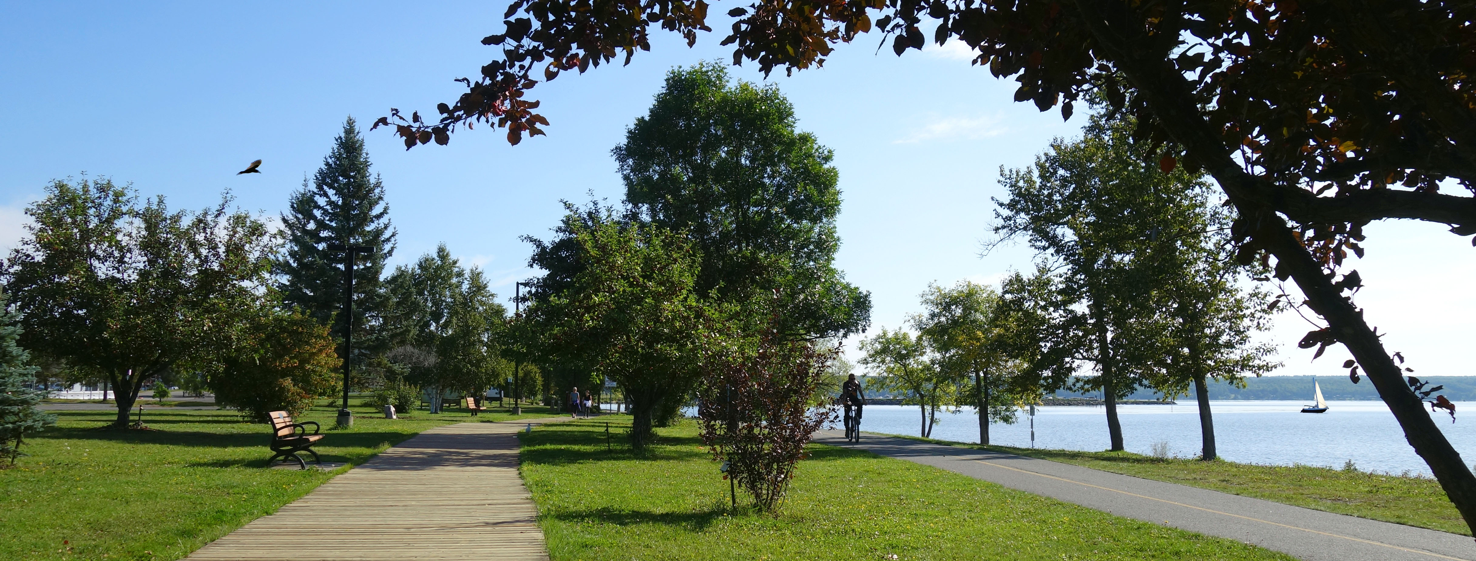 This images shows residents walking and biking on the New Liskeard boardwalk and bike path, with Lake Timiskaming in the background.