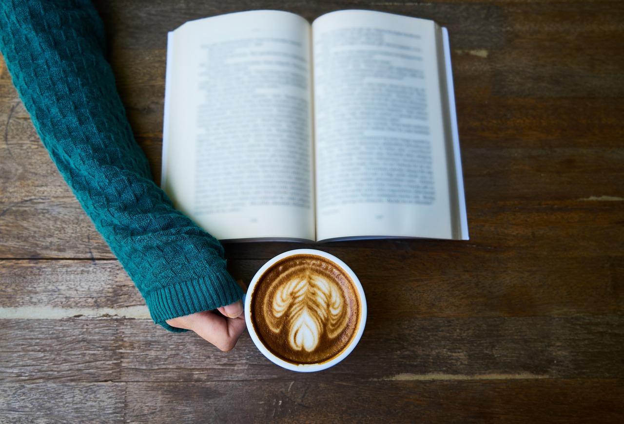 Hand holding a mug with a book set open in front of it