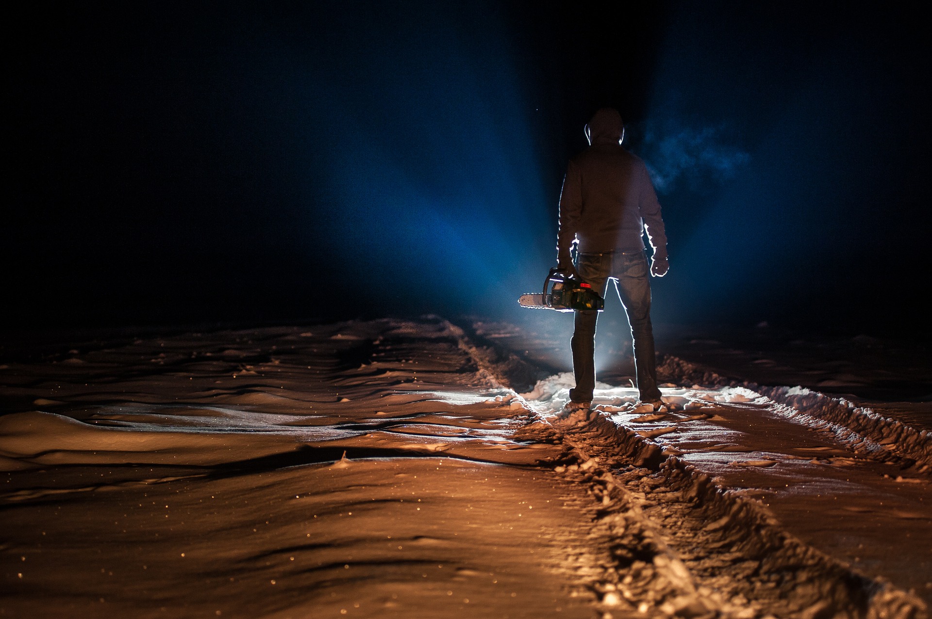 Man standing on snowy road holding a chainsaw