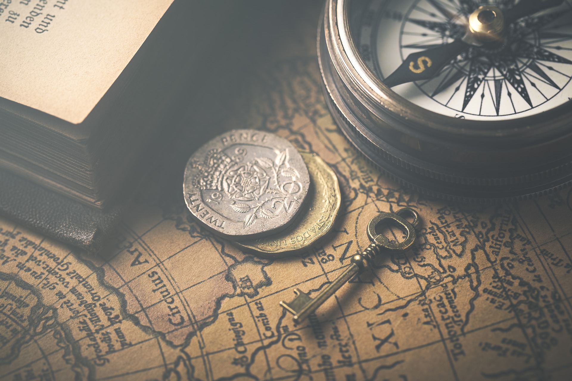 A key, compass, coins and edge of a book sitting on a map