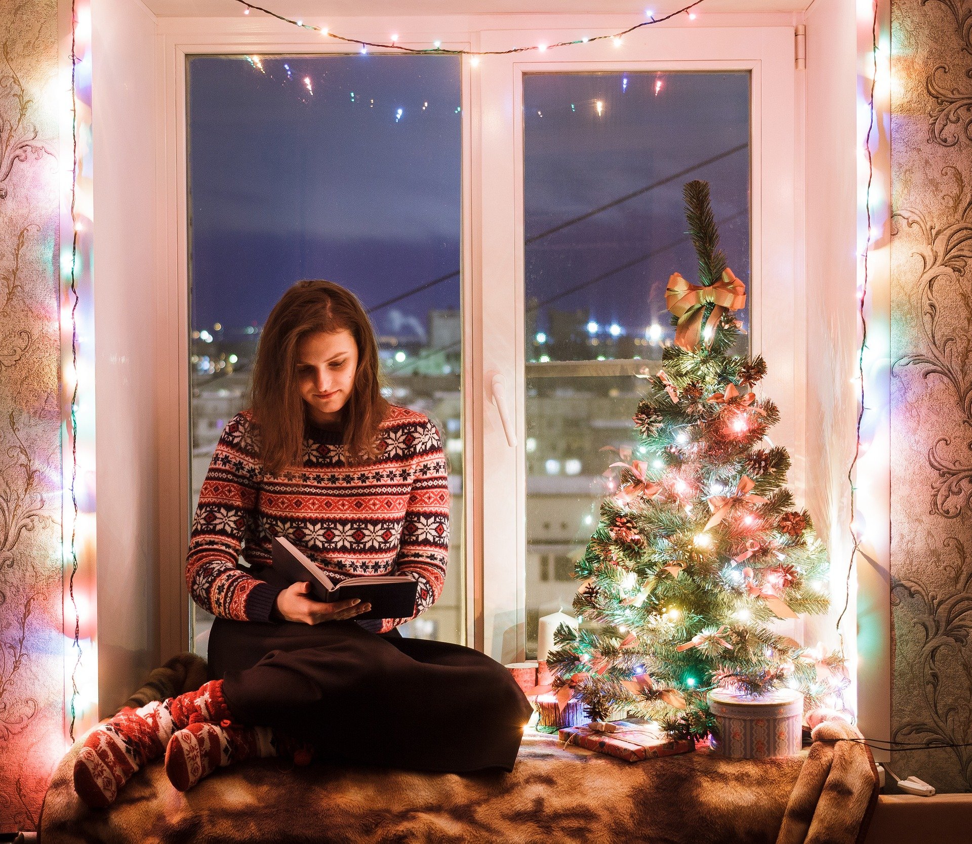 Woman reading a book in front of window with lights