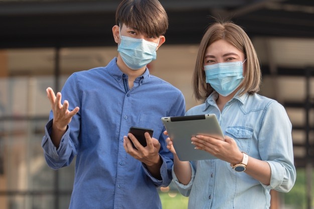Two people standing with masks on holding mobile devices